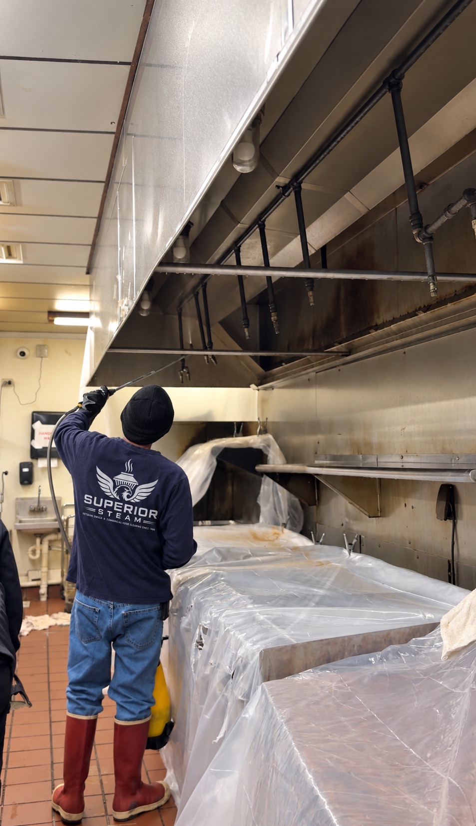 Superior Steam technician cleaning a commercial hood with the cooking equipment covered in protective plastic